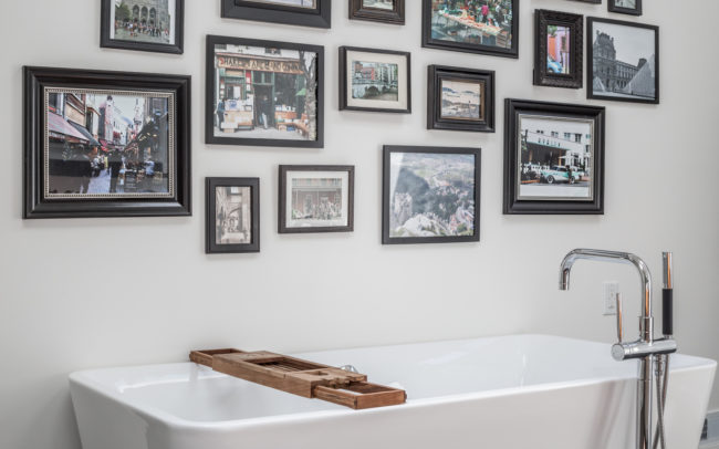 A white bathtub in a bathroom with framed pictures on the wall.