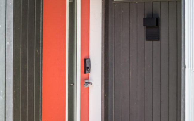 A modern front door with a red door and gray siding.